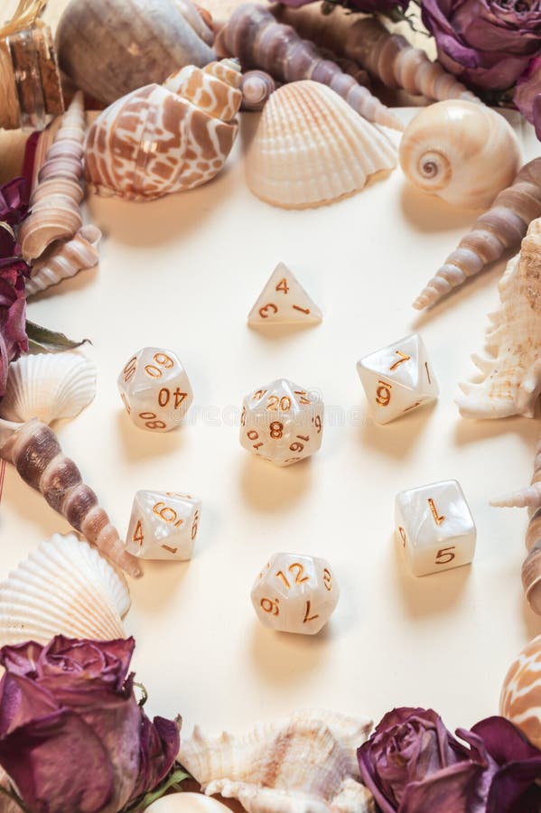 Vertical image of a set of white and gold RPG gaming dice framed by seashells and dried roses. Vertical image of a set of white and gold RPG gaming dice framed by seashells and dried roses