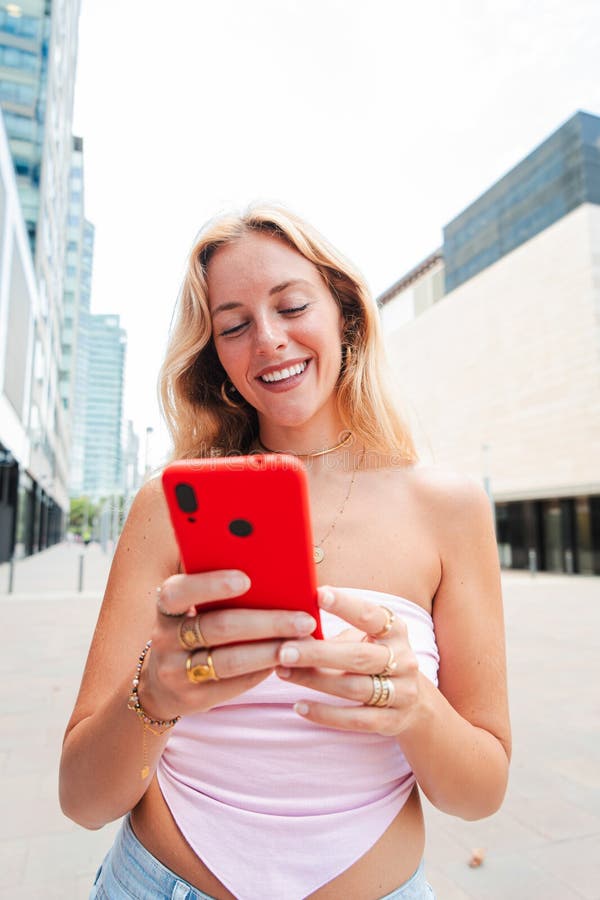 Vertical. jeune femme blonde souriante utilisant un téléphone portable en plein air profitant d'une journée ensoleillée portant un images stock