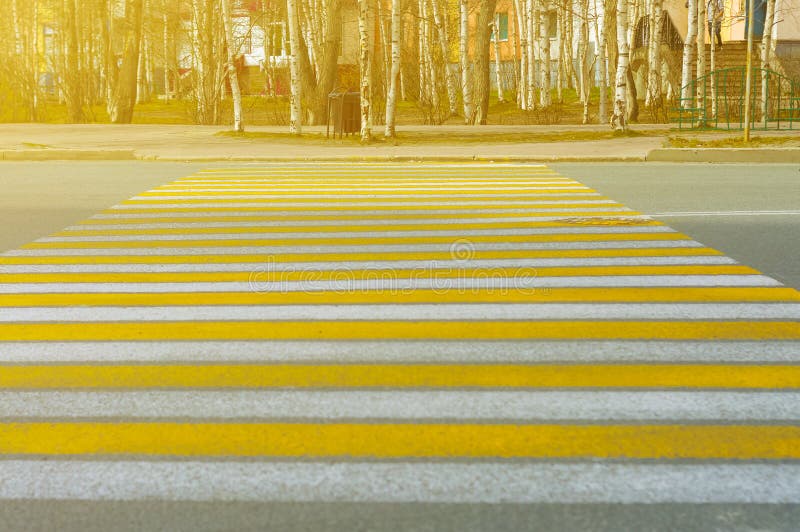 Vertical lines of road markings are white and yellow at a pedestrian crossing on a city street on a sunny evening. stock photo Vertical lines of road markings are white and yellow at a pedestrian crossing on a city street on a sunny evening. stock photo
