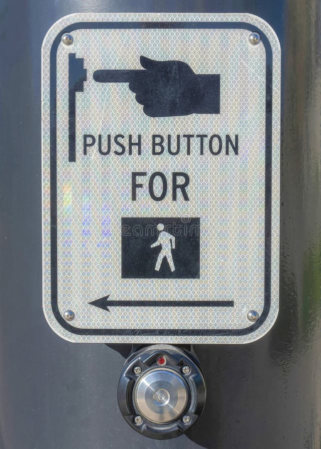 Vertical Pedestrian button on a black post at Daybreak in South Jordan, Utah. Close up of a sign with Push button for pedestrian symbol against the view of the side walk and road near the houses.