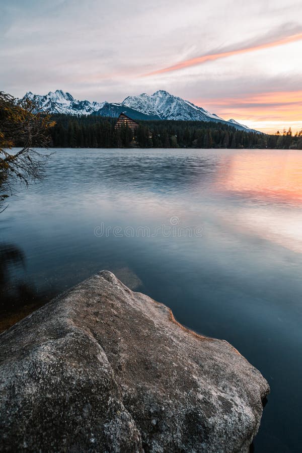 Vertical photo of beautiful lake in autumn scenery with amazing snowy mountains on background. Strbske pleso in High Tatras in