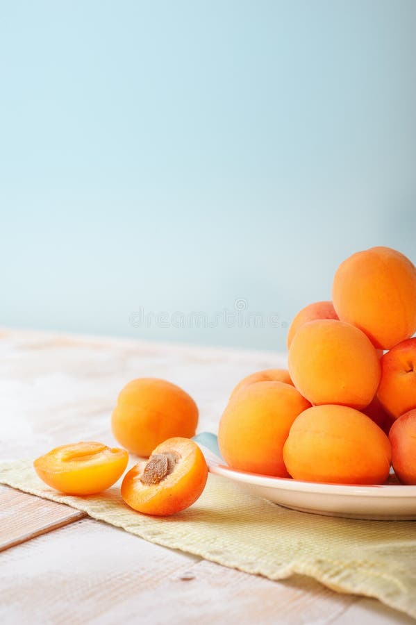 Vertical photo of Delicious ripe orange apricots in a bright plate on wooden table with green napkin on light blue wall background royalty free stock photos Vertical photo of Delicious ripe orange apricots in a bright plate on wooden table with green napkin on light blue wall background royalty free stock photos