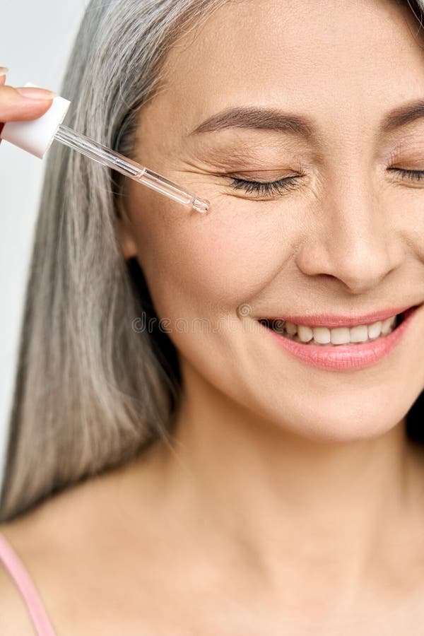 Vertical portrait of mature senior Asian woman with pipette serum essence.