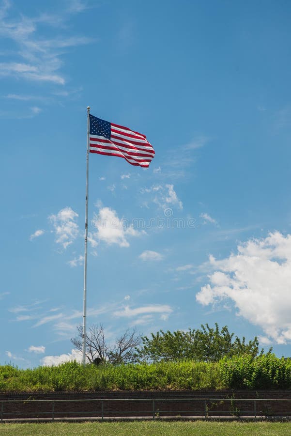 Vertical shot of an American flag waving on a pole with a blue sky background. A vertical shot of an American flag waving on a pole with a blue sky background royalty free stock image Vertical shot of an American flag waving on a pole with a blue sky background. A vertical shot of an American flag waving on a pole with a blue sky background royalty free stock image