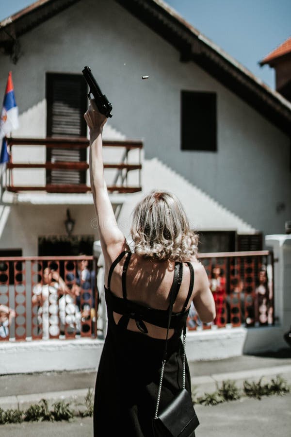 Vertical shot of a back of a blonde female in a mini dress holding a pistol and shooting it up stock photography Vertical shot of a back of a blonde female in a mini dress holding a pistol and shooting it up stock photography