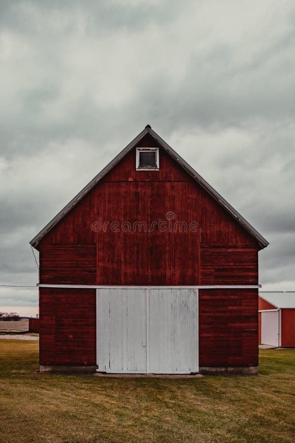 Vertical shot of a beautiful red wooden barn with a white door on a grass-covered field