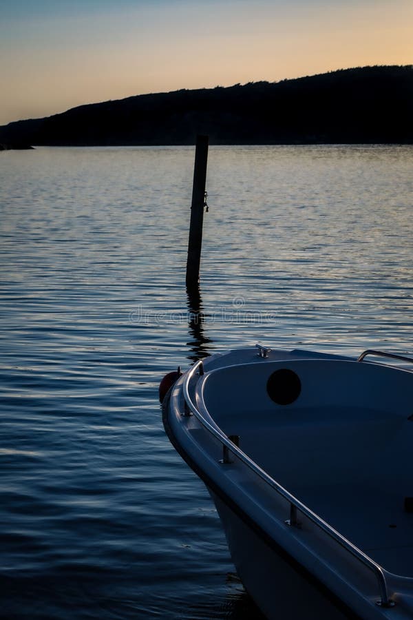 Vertical shot of a docked boat with silhouette view of a cliff in the background at sunset royalty free stock image