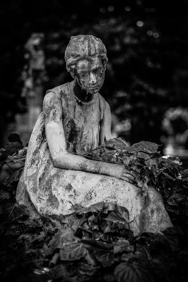 Vertical Shot Of A Female Statue Surrounded By Leaves In Black And White