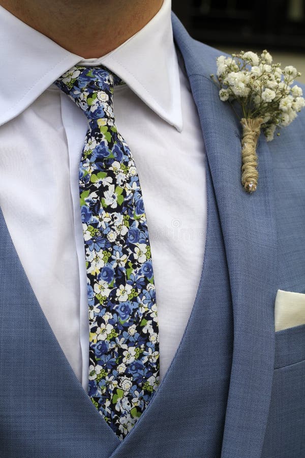 Vertical shot of a groom wearing a blue three-piece suit with a stylish tie with a floral print