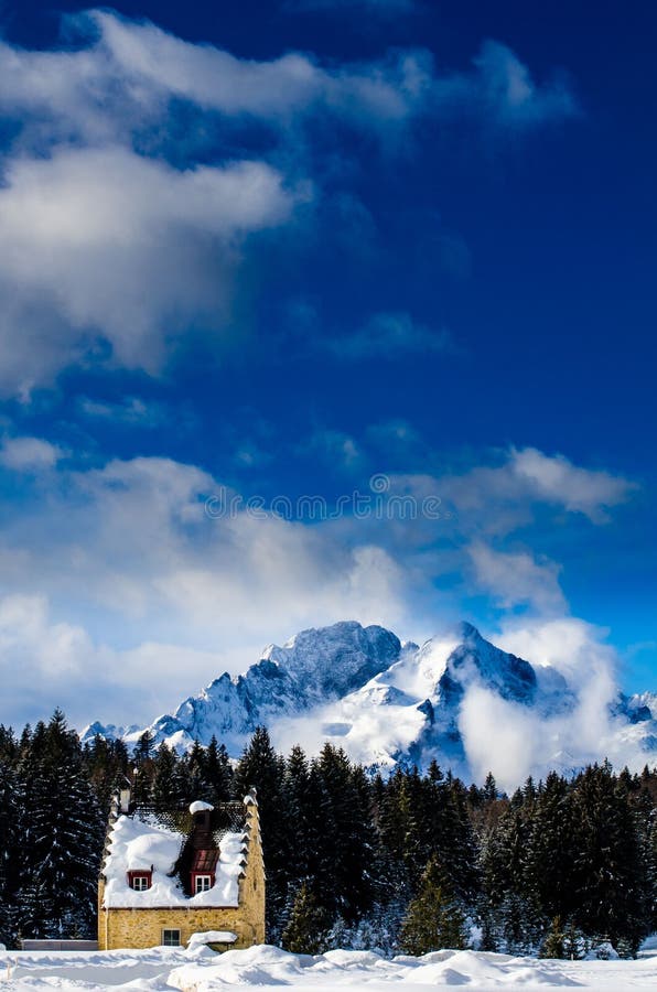 Vertical Shot of a Small House in Snow with a Forest and Mountains in