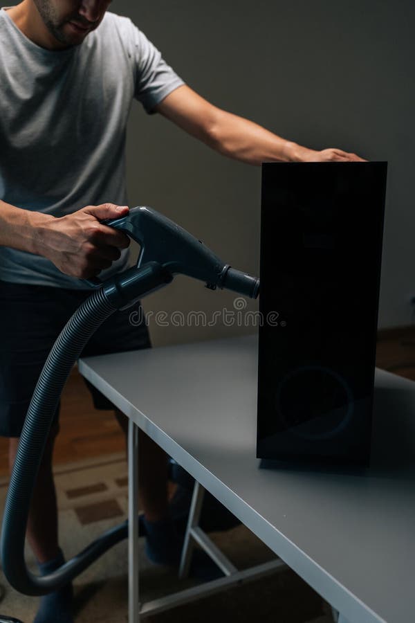 Vertical shot of technician male using vacuum cleaner to remove dust and debris from ventilation holes of computer case stock photography