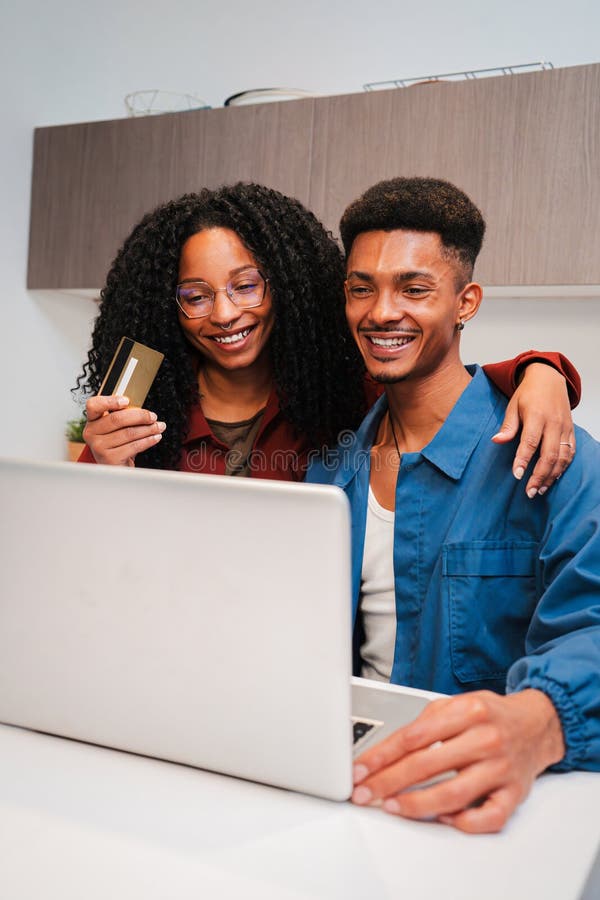 Vertical. un couple afro-américain souriant magasine en ligne avec un ordinateur portable et tient une carte de crédit partageant photo stock