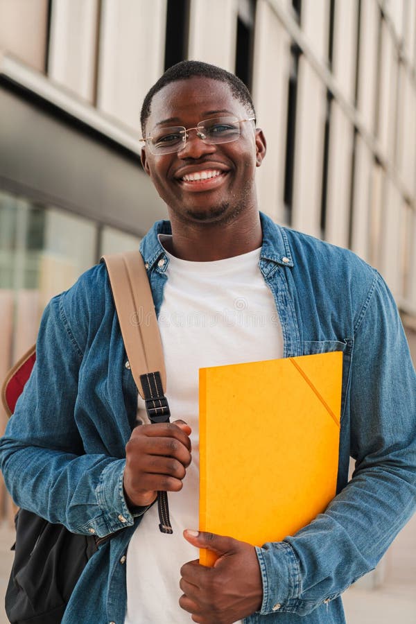 Vertical. un étudiant afro-américain souriant regardant la caméra tenant un dossier et portant un sac à dos debout photos libres de droits