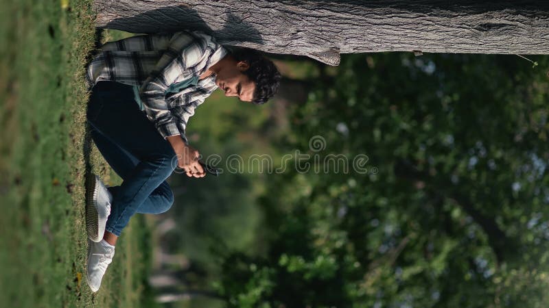 VERTICAL VIDEO POV pensive Arabic guy mobile phone relaxing outdoor nature summer sunny garden park stock footage