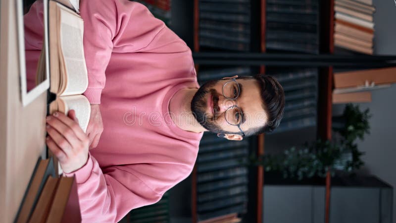 VERTICAL VIDEO POV smiling Latino modern bearded man reading book at library posing desk workplace stock video footage