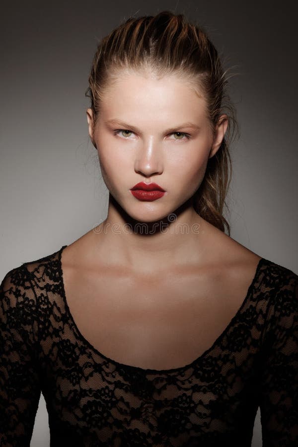 Close up frontal portrait of a beautiful blonde girl with hair gathered in a ponytail, red lips, on dark background.