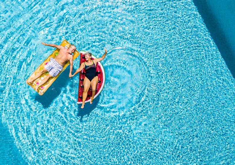 Vertical view of happy couple of old senior people enjoying the summer holiday vacation at the blue water pool with coloured treny