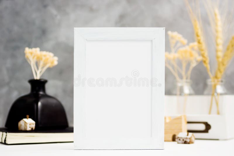 Vertical white Photo frame mock up with dry plants in vase, notebook and wooden houses on shelf. Scandinavian style stock image