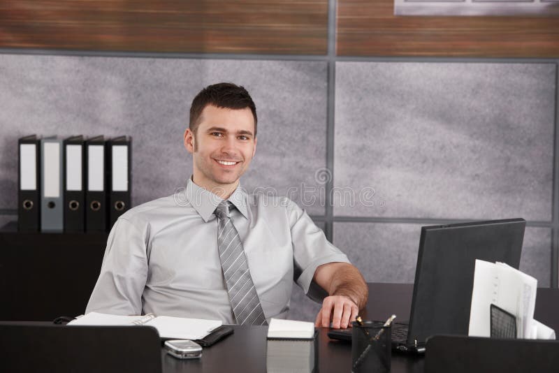 Portrait of casual businessman sitting at desk wearing short sleeved shirt, smiling. Copyspace on right. Portrait of casual businessman sitting at desk wearing short sleeved shirt, smiling. Copyspace on right.