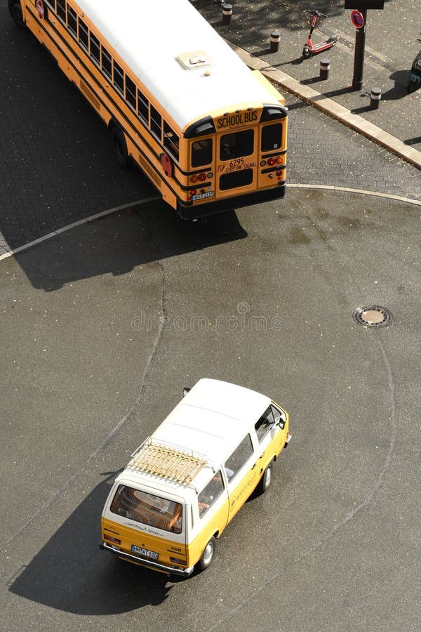 Vertikalaufnahme eines gelb-weißen Autos hinter einem amerikanischen Schulbus auf der Straße