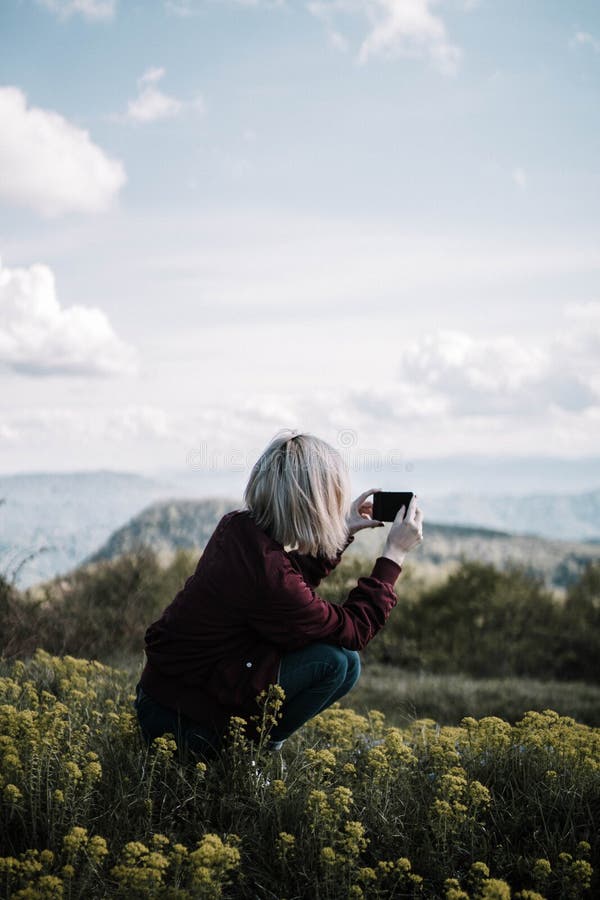 Vertikale geschossene Frau, die auf einem schönen Blumengebiet hockt und Fotos an ihrem Telefon macht stockfotos Vertikale geschossene Frau, die auf einem schönen Blumengebiet hockt und Fotos an ihrem Telefon macht stockfotos