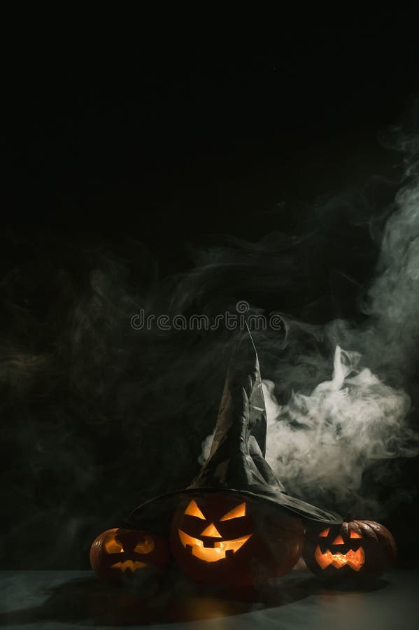 Vertikale Halloween-Karte. Hexenhut auf einem Gefäß mit geschnitzten gruseligen Grimassen auf einem schwarzen Hintergrund im Nebel lizenzfreie stockbilder