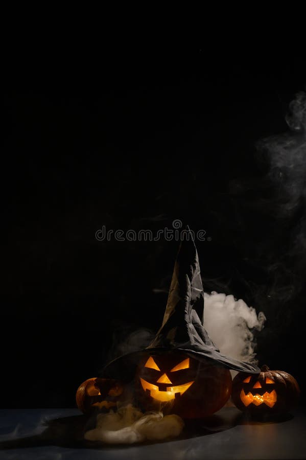 Vertikale Halloween-Karte. Hexenhut auf einem Gefäß mit geschnitzten gruseligen Grimassen auf einem schwarzen Hintergrund im Nebel lizenzfreie stockfotografie