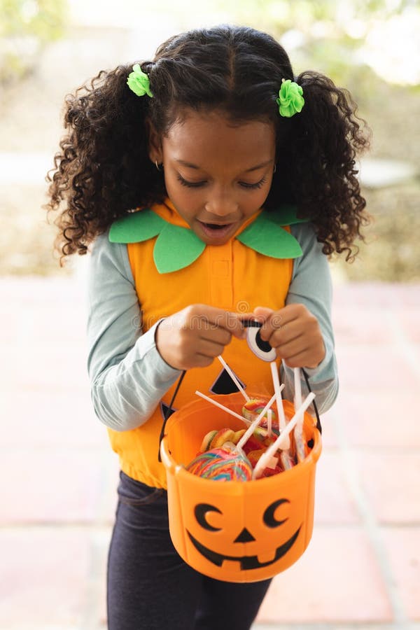 Vertikales Bild eines glücklichen afrikanischen amerikanischen Mädchens in halloween Kostüm mit Korb stockfotografie