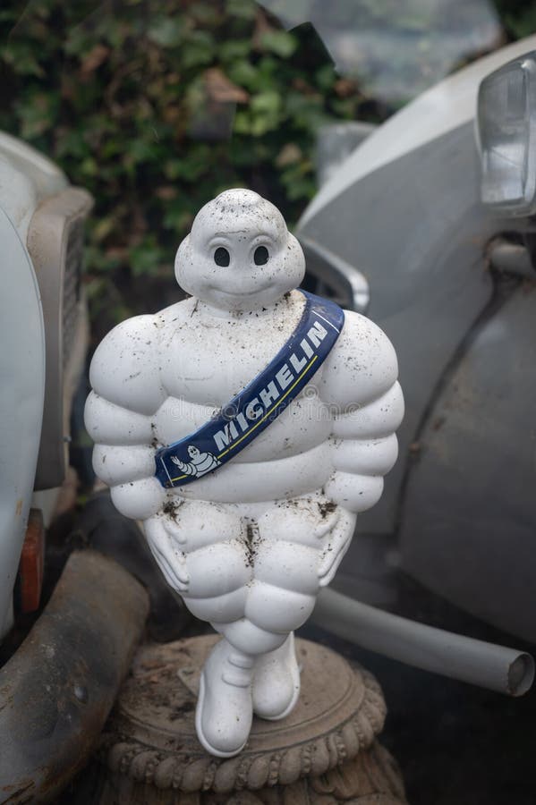 A vertical shot of the old Michelin tire doll between two abandoned cars. A vertical shot of the old Michelin tire doll between two abandoned cars