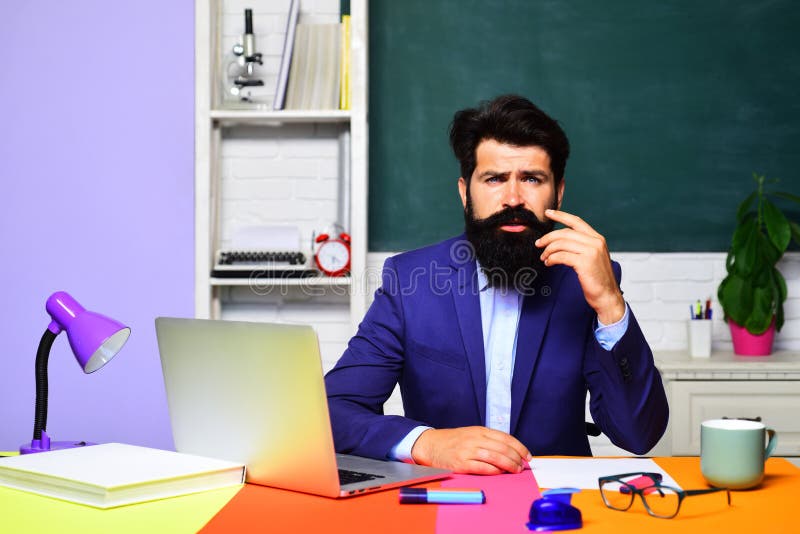 Verwirrte männliche Lehrerin oder Studentin, die im Klassenzimmer sitzt. zurück zur Schule. Lehrer arbeitet mit Laptop stockbild