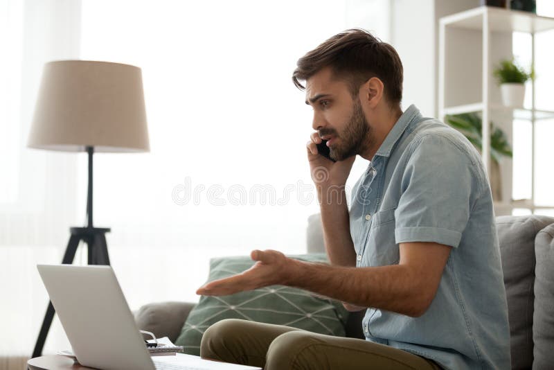 Verwirrter Mann sprechen am Telefon, das Laptopbetriebsprobleme löst stockfotos