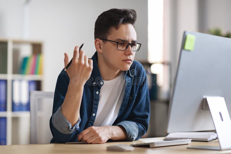 Verwirrter männlicher Büroangestellter, der am Arbeitsplatz sitzt und sich den Bildschirm anschaut stockbilder
