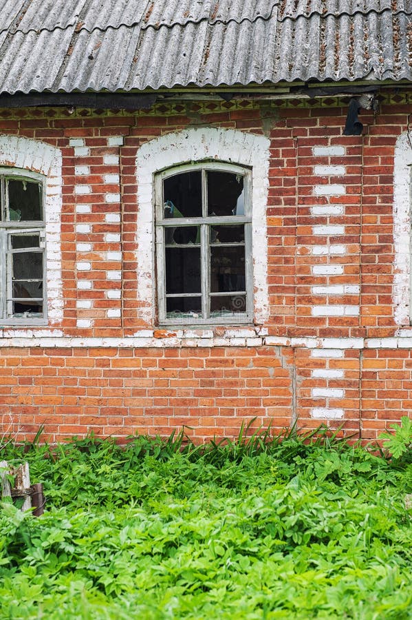 Verwittertes Ziegelhaus mit zerschmetterten Fenstern, abgelegen im Grünen lizenzfreie stockfotos