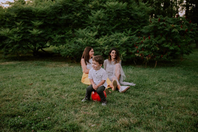 Very cute two years boy make funny faces in front of the camera while on the background two ladies smiling large and stock photography Very cute two years boy make funny faces in front of the camera while on the background two ladies smiling large and stock photography