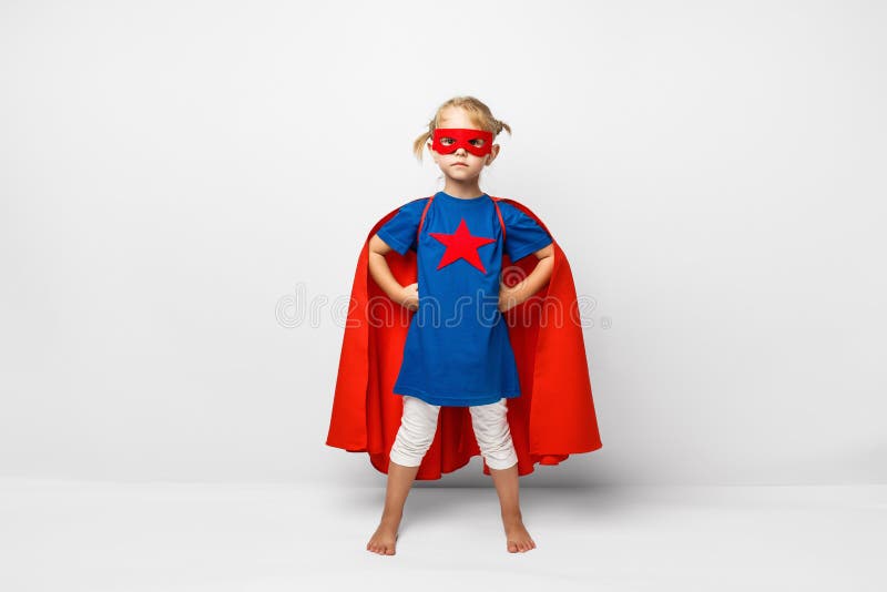 Very excited little girl dressed like superhero jumping alongside the white wall.