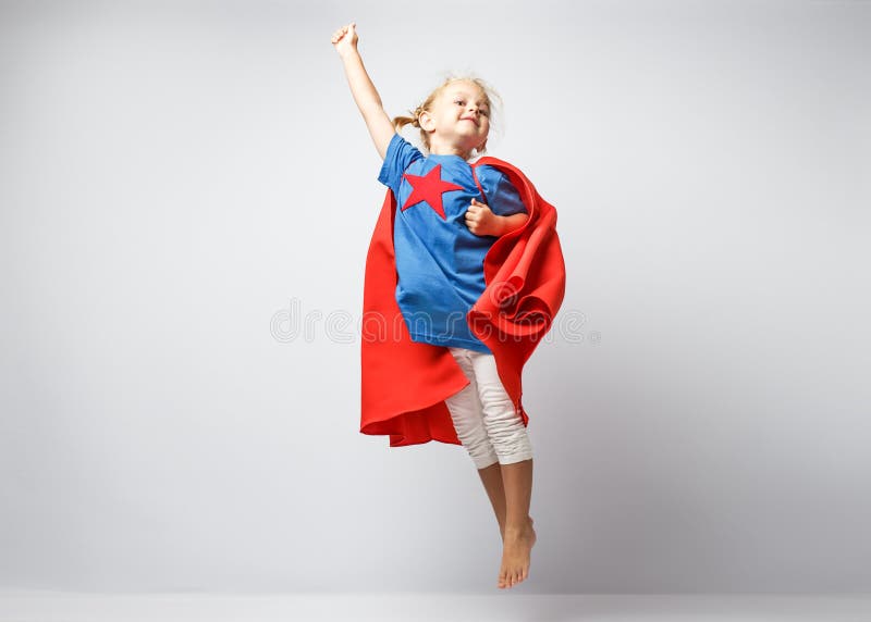 Very excited little girl dressed like superhero jumping alongside the white wall.