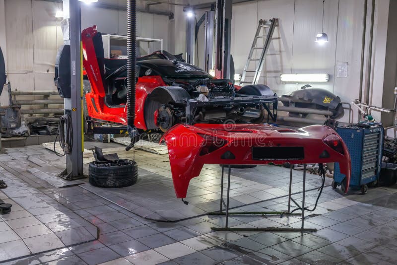 Very expensive and powerful sports car of red color, disassembled for repair, lifted on a lift in auto service, next to it is a royalty free stock photography Very expensive and powerful sports car of red color, disassembled for repair, lifted on a lift in auto service, next to it is a royalty free stock photography