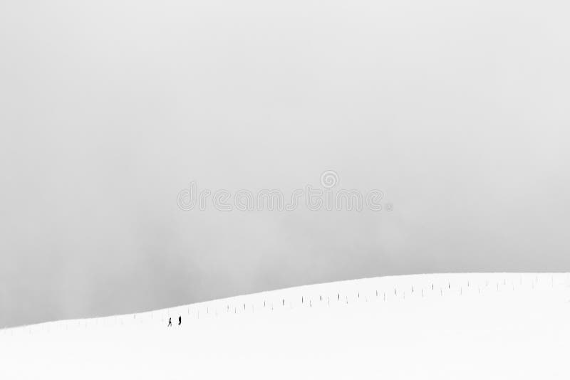 A very minimalistic view of two distant people over a mountain covered by snow, near a fence