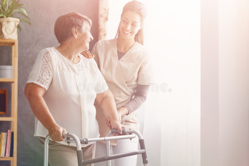 Smiling pretty caregiver and old lady with walker at nursing home. Smiling pretty caregiver and old lady with walker at nursing home