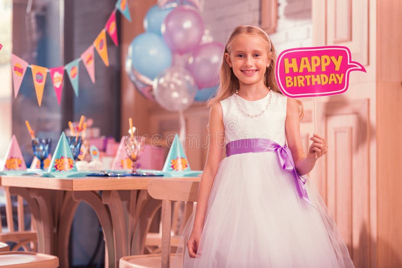 Vestido branco vestindo da menina bonito e guardar o sinal do feliz aniversario imagem de stock Vestido branco vestindo da menina bonito e guardar o sinal do feliz aniversario imagem de stock