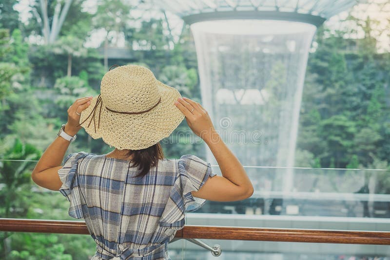 Vestido e chapéu azul do desgaste de jovem mulher, posição asiática do viajante e vista ao redemoinho bonito da chuva no aeroport foto de stock Vestido e chapéu azul do desgaste de jovem mulher, posição asiática do viajante e vista ao redemoinho bonito da chuva no aeroport foto de stock
