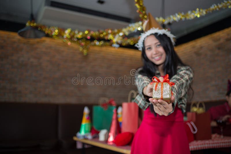 Vestido rojo del desgaste de mujer y sombrero de Papá Noel que muestra la caja de regalo de oro a mano en restaurante concepto de fotografía de archivo libre de regalías Vestido rojo del desgaste de mujer y sombrero de Papá Noel que muestra la caja de regalo de oro a mano en restaurante concepto de fotografía de archivo libre de regalías
