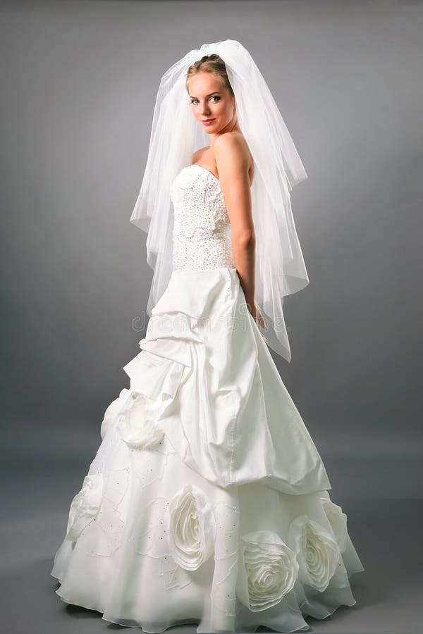 Confident young bride wearing gorgeous gown standing on neutral studio background side view. Confident young bride wearing gorgeous gown standing on neutral studio background side view