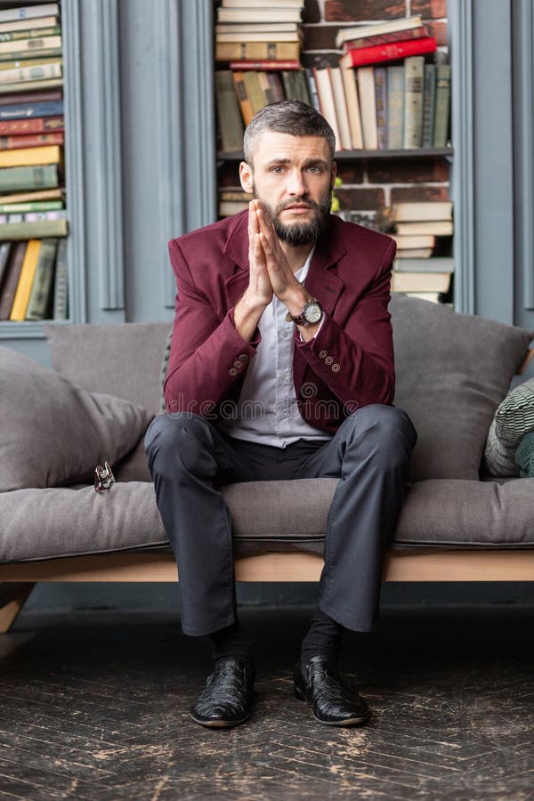 Vestir à moda considerável do homem de negócios escuro - revestimento vermelho que senta-se no sofá fotografia de stock Vestir à moda considerável do homem de negócios escuro - revestimento vermelho que senta-se no sofá fotografia de stock