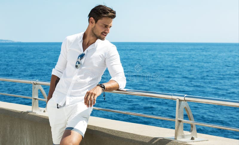 Vestiti bianchi d'uso dell'uomo bello che posano nel paesaggio del mare
