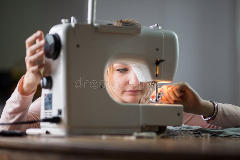 Vestiti di cucito della bella giovane donna con la macchina per cucire fotografia stock Vestiti di cucito della bella giovane donna con la macchina per cucire fotografia stock