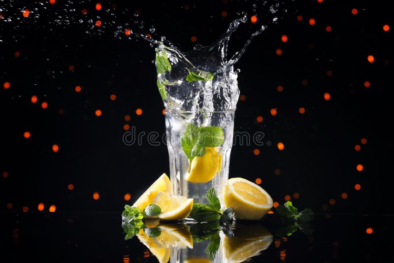 Vetro con la spruzzatura acqua e del limone contro le luci vaghe immagini stock Vetro con la spruzzatura acqua e del limone contro le luci vaghe immagini stock