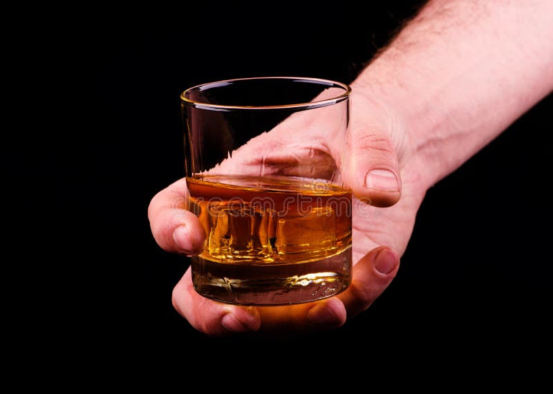Vetro del whiskey in una mano di un uomo su fondo nero, brandy in un vetro fotografia stock libera da diritti Vetro del whiskey in una mano di un uomo su fondo nero, brandy in un vetro fotografia stock libera da diritti