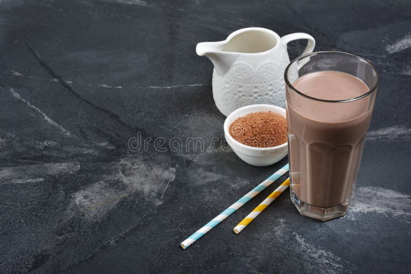 Vetro della bevanda fredda deliziosa del latte al cioccolato con la brocca ed il cacao in polvere bianchi fotografie stock Vetro della bevanda fredda deliziosa del latte al cioccolato con la brocca ed il cacao in polvere bianchi fotografie stock