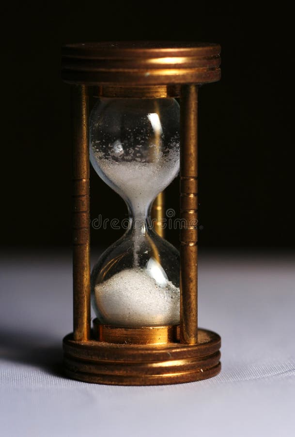 A small sand glass in golden retro style measuring and showing the time: the white sand is running down from the upper glass to the bottom. A small sand glass in golden retro style measuring and showing the time: the white sand is running down from the upper glass to the bottom